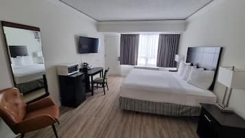 Habitación de hotel con una cama grande, un escritorio con computadora, televisor y ventana con cortinas.