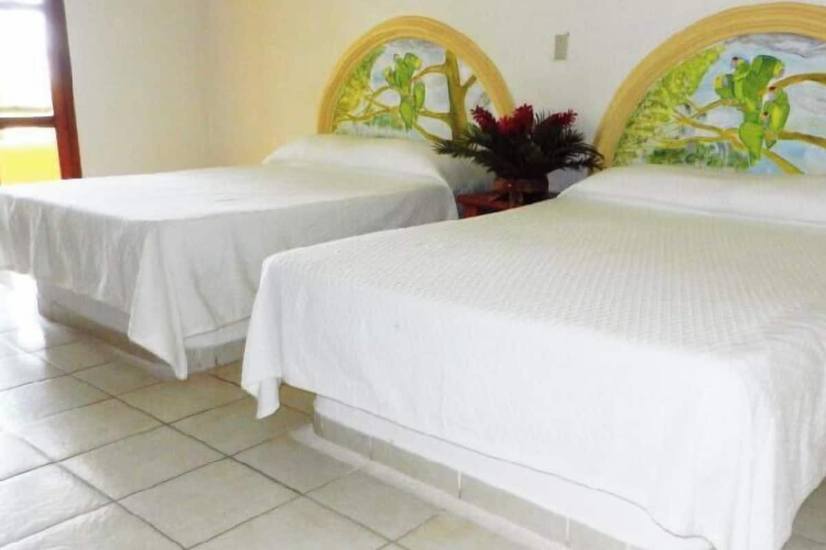 Two single beds with white linens, a tiled floor, and a painting on the headboard.