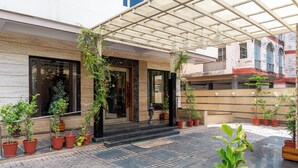 A modern building with a covered entrance, potted plants, and a paved courtyard. - Amantra Comfort Hotel (Udaipur)
