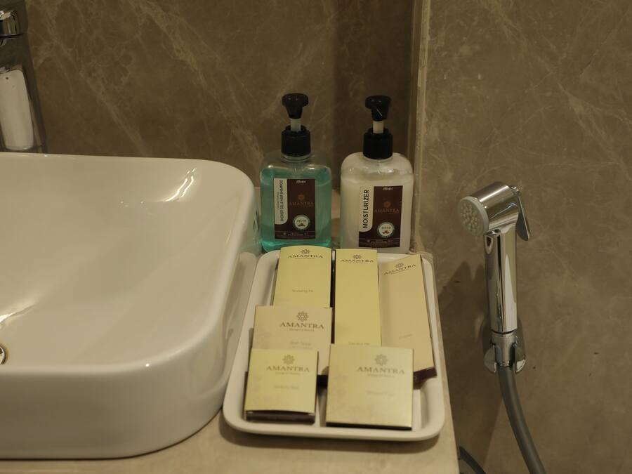 Un baño con un lavamanos blanco, dos botellas de jabón para manos y un cabezal de ducha.
