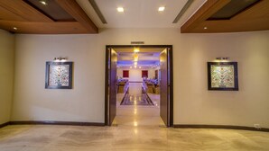 A hallway leading to a conference hall with framed artwork on the walls and a polished marble floor. - Amantra Comfort Hotel (Udaipur)