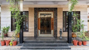 A hotel entrance with a marble facade, a wooden door, and potted plants. - Amantra Comfort Hotel (Udaipur)