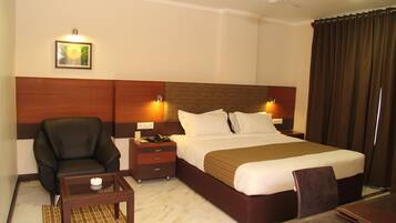 A hotel room with a large bed, a chair, a small table, a nightstand, and a ceiling fan.