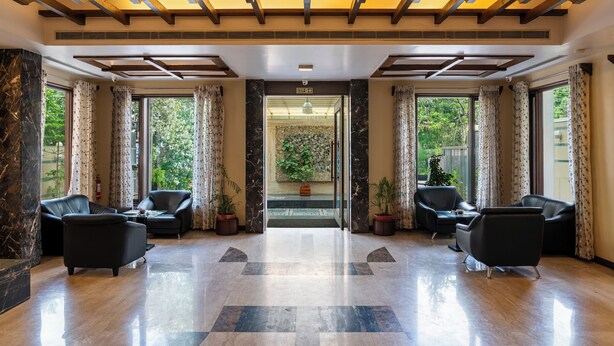 A lobby with a marble floor, black leather chairs, and large windows with curtains. - Amantra Comfort Hotel (Udaipur)