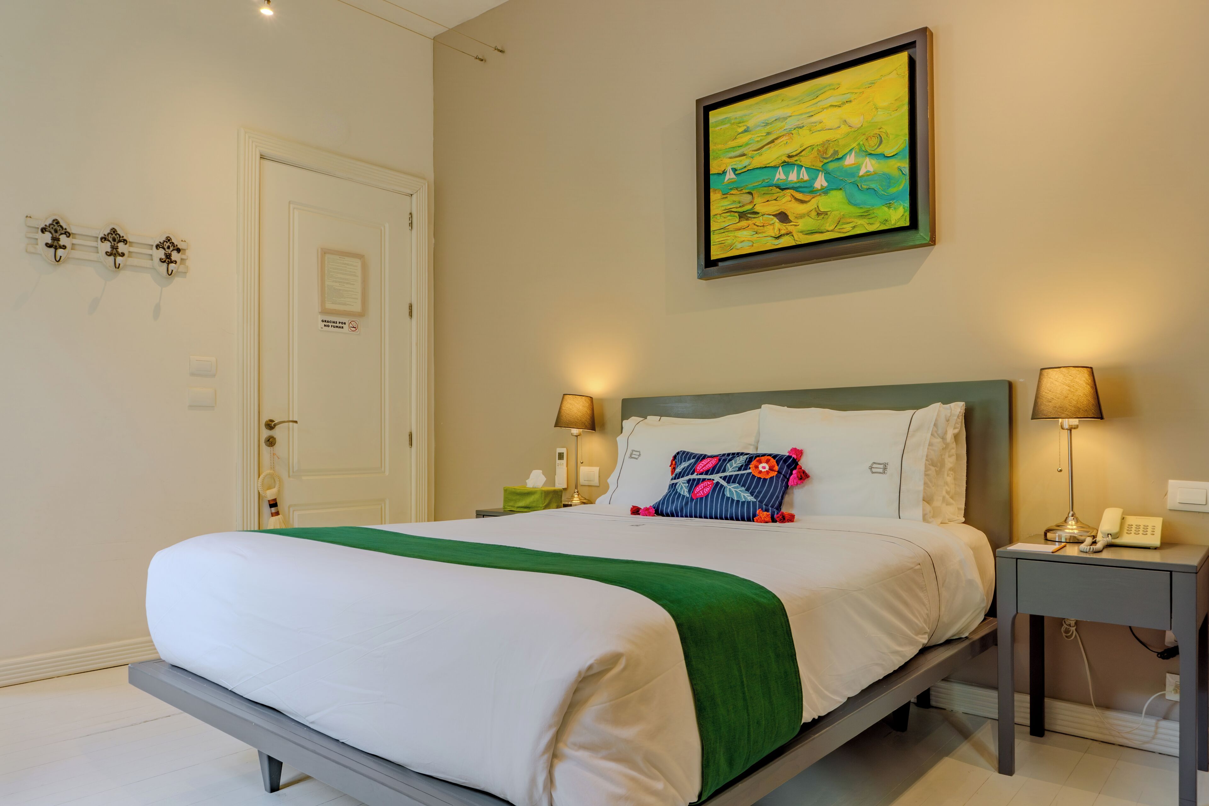 Habitación de hotel con cama, lámparas de noche, un cuadro, una puerta y un interruptor de luz en la pared.