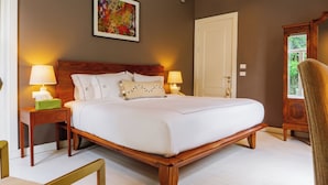 A hotel room with a large bed, two bedside lamps, a framed artwork on the wall, a door, and a window with a view of greenery. - Hotel Villa Condesa (Mexico City)