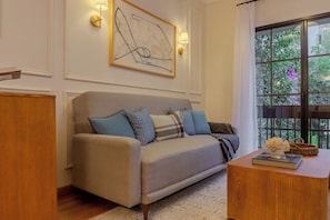 A living room with a sofa, a coffee table, and a window with a view of greenery. - Hotel Villa Condesa (Mexico City)