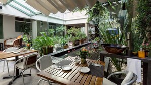 Un jardín interior con mesas y sillas, plantas en macetas y una fuente de agua.