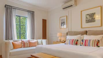 Habitación de hotel con cama, sofá, mesita de noche con lámpara y ventana con cortinas.