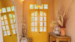 A yellow door with multiple windows, a hanging light fixture, and a small table with a vase of dried plants. - Hotel Villa Condesa (Mexico City)