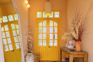 A yellow door with multiple windows, a hanging light fixture, and a small table with a vase of dried plants.