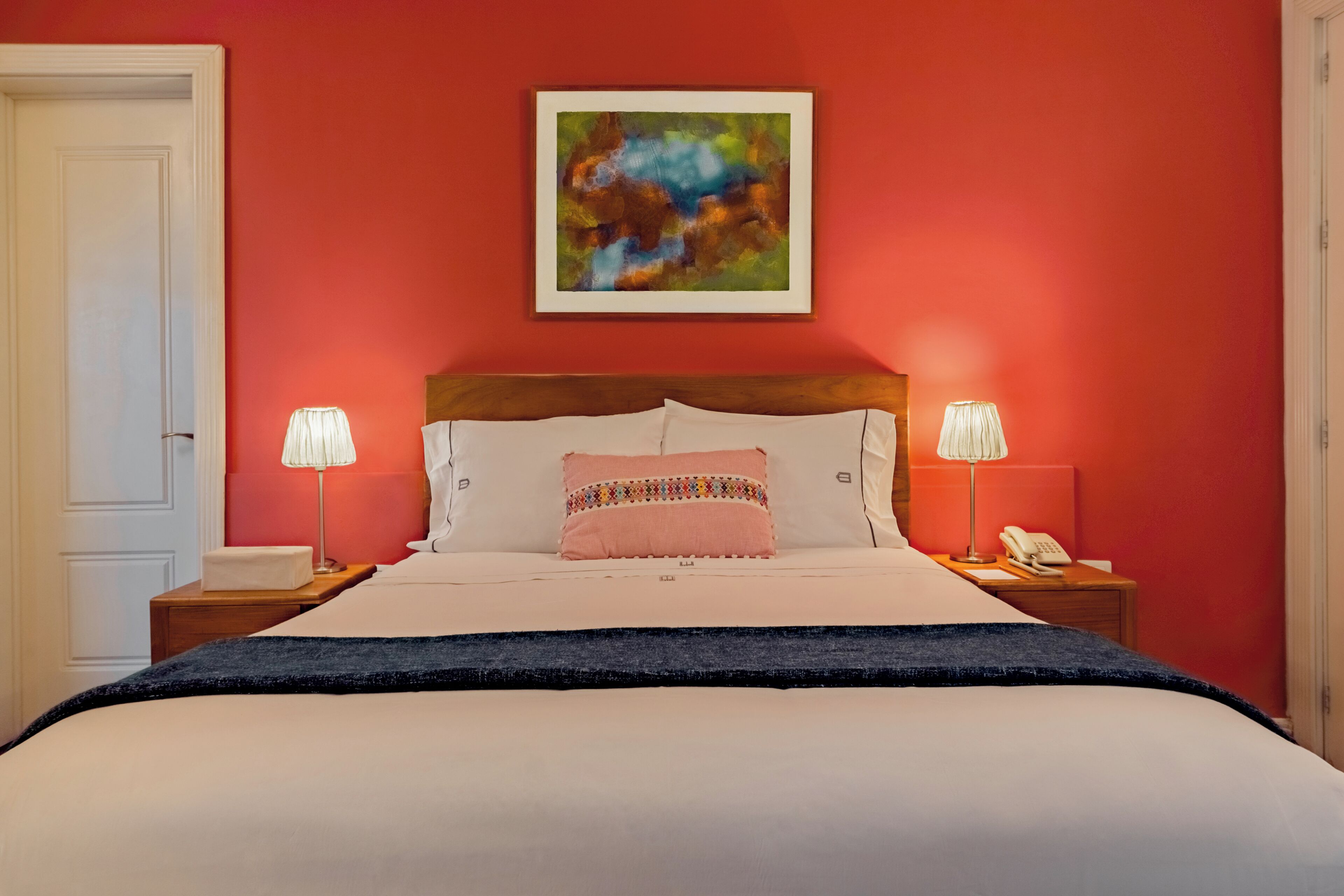Quarto de hotel com uma cama grande, duas luminárias de cabeceira, um telefone e um quadro na parede.