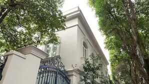 Un edificio con fachada blanca, una reja de hierro negro y árboles al fondo.