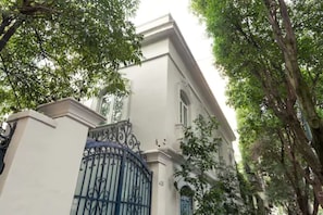 A building with a white facade, a black wrought iron gate, and trees in the background.