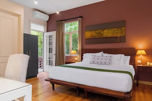 A hotel room with a bed, bedside table, lamp, and a view of greenery through the window. - Hotel Villa Condesa (Mexico City)