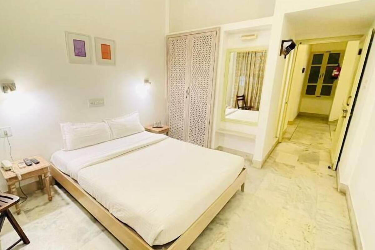 A bedroom with a bed, bedside tables, a chair, a wardrobe, and a door leading to another room.