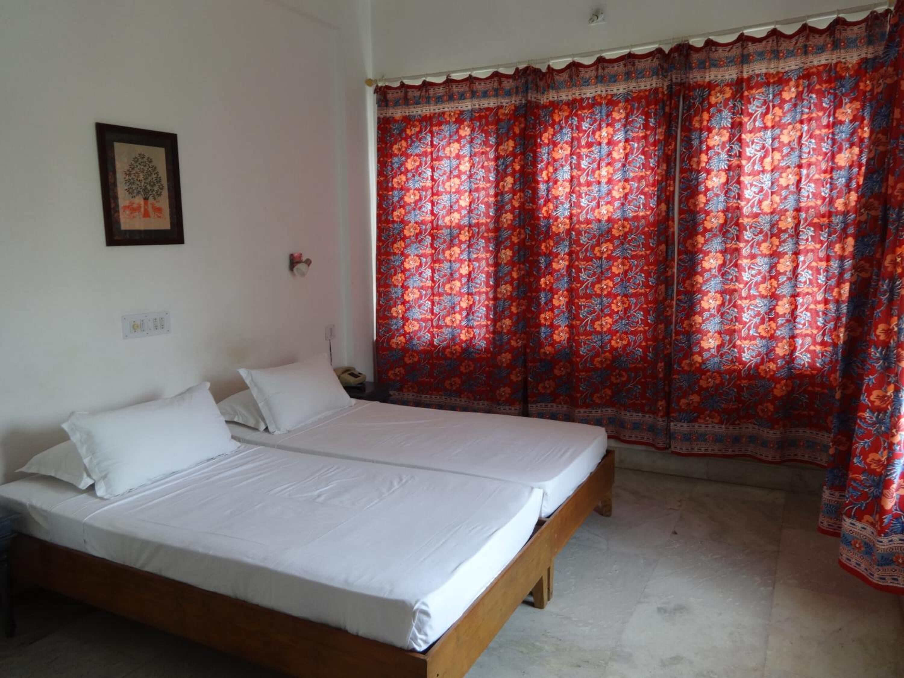 A double bed with white linens in a room with a red floral curtain.