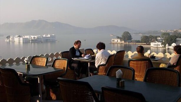 A restaurant with outdoor seating overlooking a lake, featuring tables and chairs arranged for dining. - Jaiwana Haveli (Udaipur)