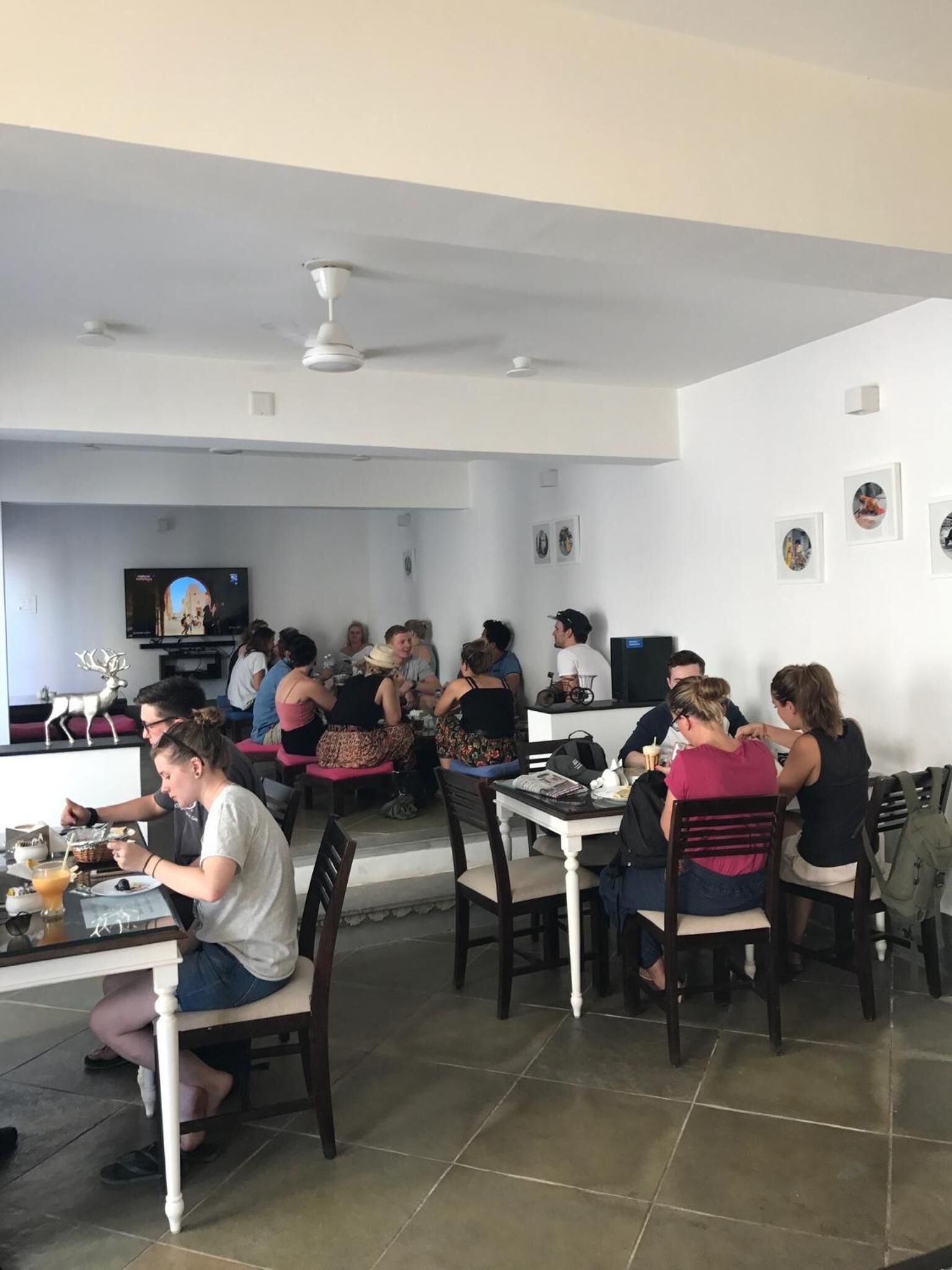 A spacious dining area with multiple tables and chairs, a television screen, and framed pictures on the walls.