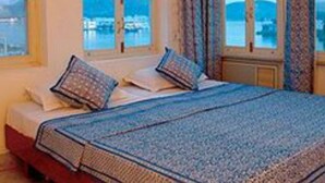 A room with a bed, large windows with curtains, and a view of a body of water. - Jaiwana Haveli (Udaipur)