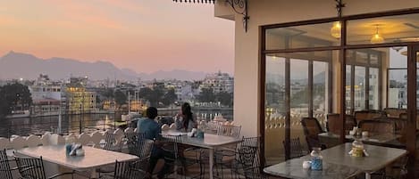 Un área de estar al aire libre con mesas y sillas, con vista a un paisaje urbano y montañas.