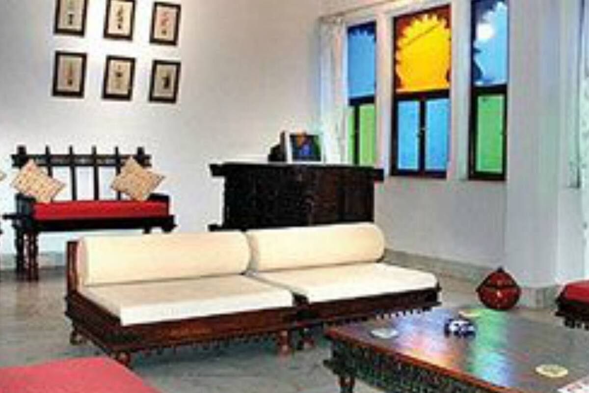 A room with a sofa, a table, and a bench. There are framed pictures on the wall and a window with colorful panes.