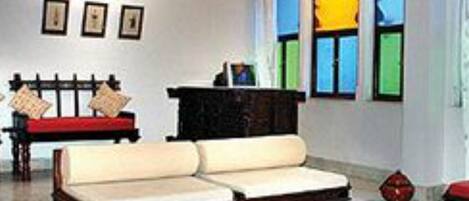 A room with a sofa, a table, and a bench. There are framed pictures on the wall and a window with colorful panes.