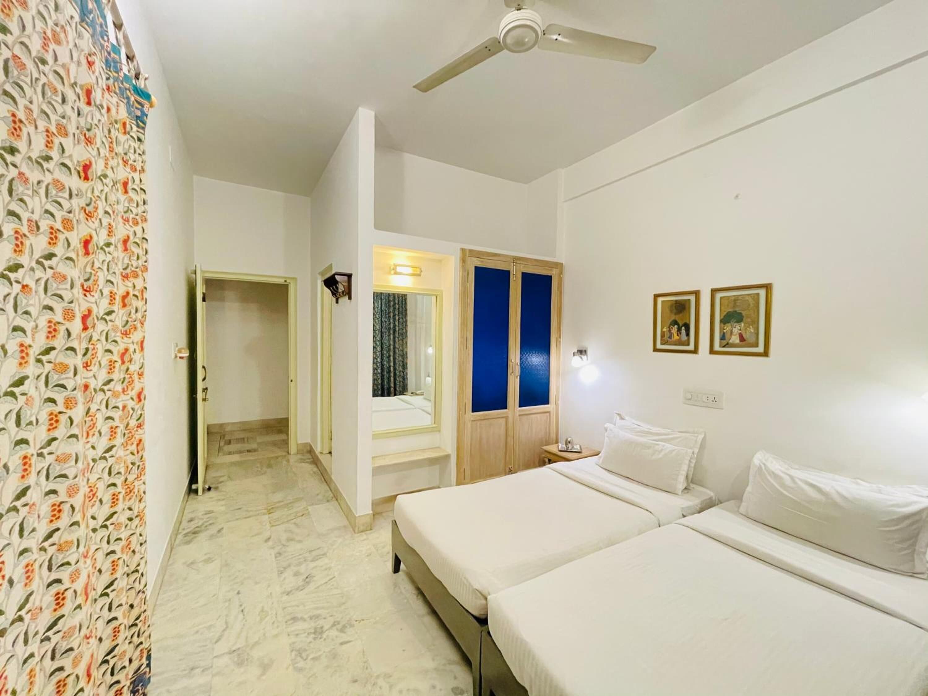 A hotel room with two beds, a wardrobe, a mirror, and a ceiling fan.