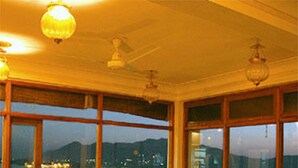 A dining area with tables and chairs, large windows with a view of a body of water and distant mountains, and hanging light fixtures. - Jaiwana Haveli (Udaipur)