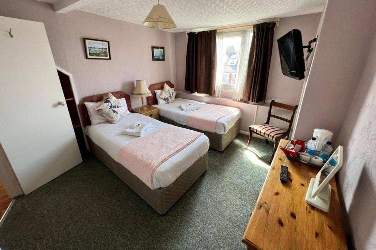 A hotel room with two single beds, a wooden desk with a chair, a lamp, and a television on the wall.