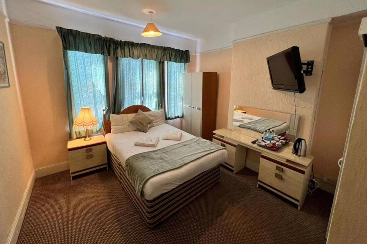 A hotel room with a bed, bedside tables, a desk, a mirror, a television, and curtains.