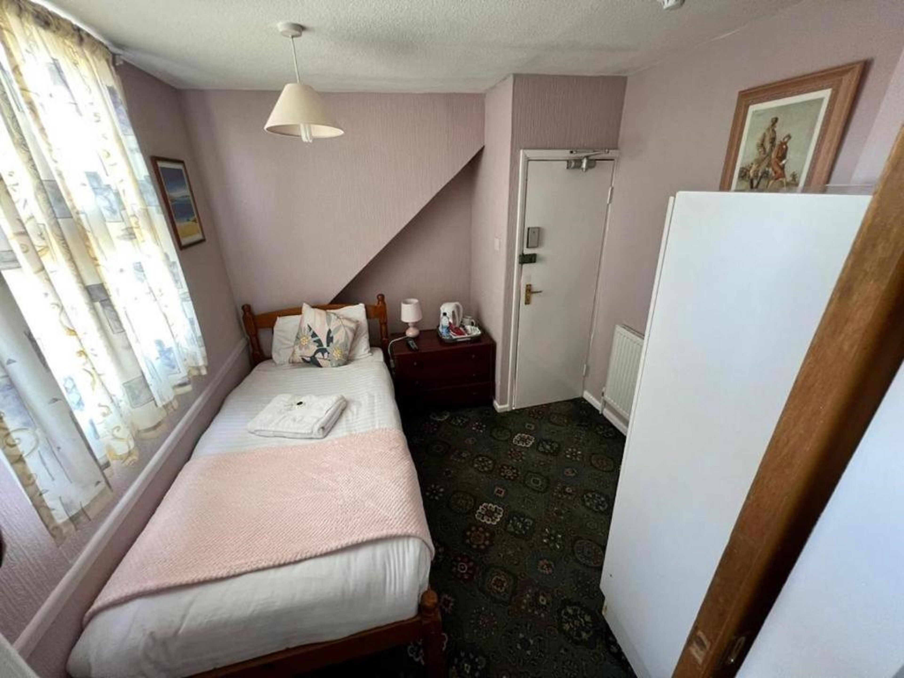 A bedroom with a bed, a nightstand, a lamp, a door, and a window with curtains.