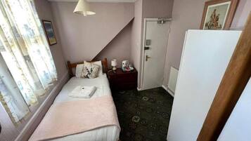 A bedroom with a bed, a nightstand, a lamp, a door, and a window with curtains.