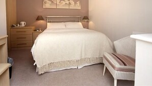 A bedroom with a bed, bedside tables, a lamp, a chair, and a wall-mounted artwork. - Blossom House Bed & Breakfast (Buxton)