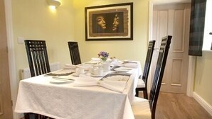 A dining table set with white tablecloth, plates, and cutlery, flanked by chairs with dark wooden frames and light-colored cushions. - Blossom House Bed & Breakfast (Buxton)