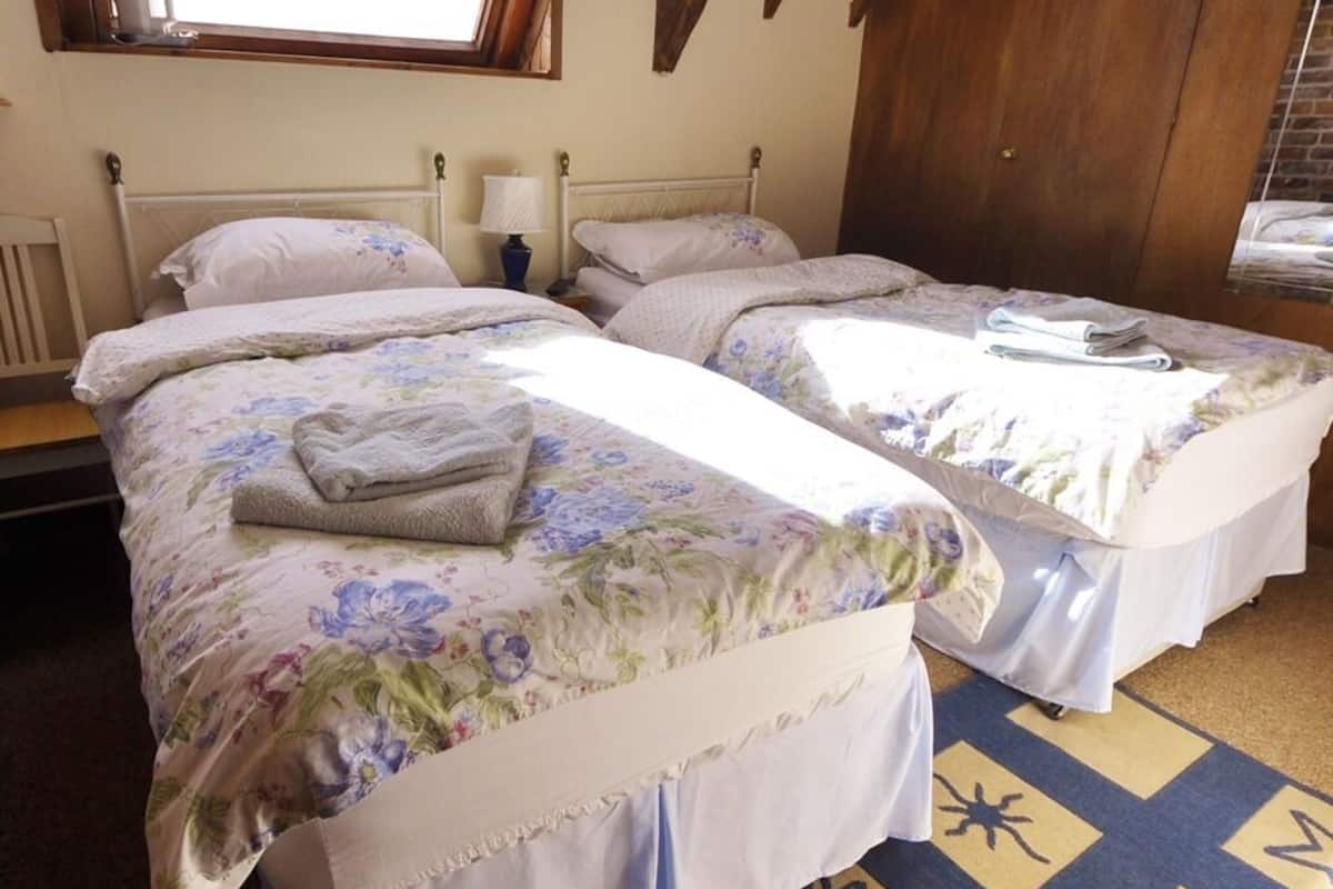 Two single beds with floral bedding, a nightstand with a lamp, and a wooden ceiling.