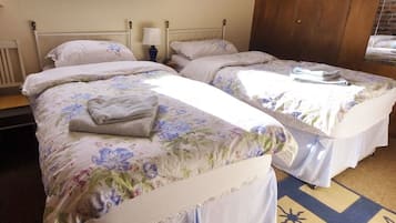 Two single beds with floral bedding, a nightstand with a lamp, and a wooden ceiling.