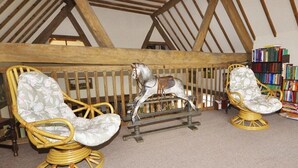 A room with a sloped ceiling, wooden beams, two wicker rocking chairs with floral upholstery, a small rocking horse, and a bookshelf with books. - Bluebell Farm (Worcester)
