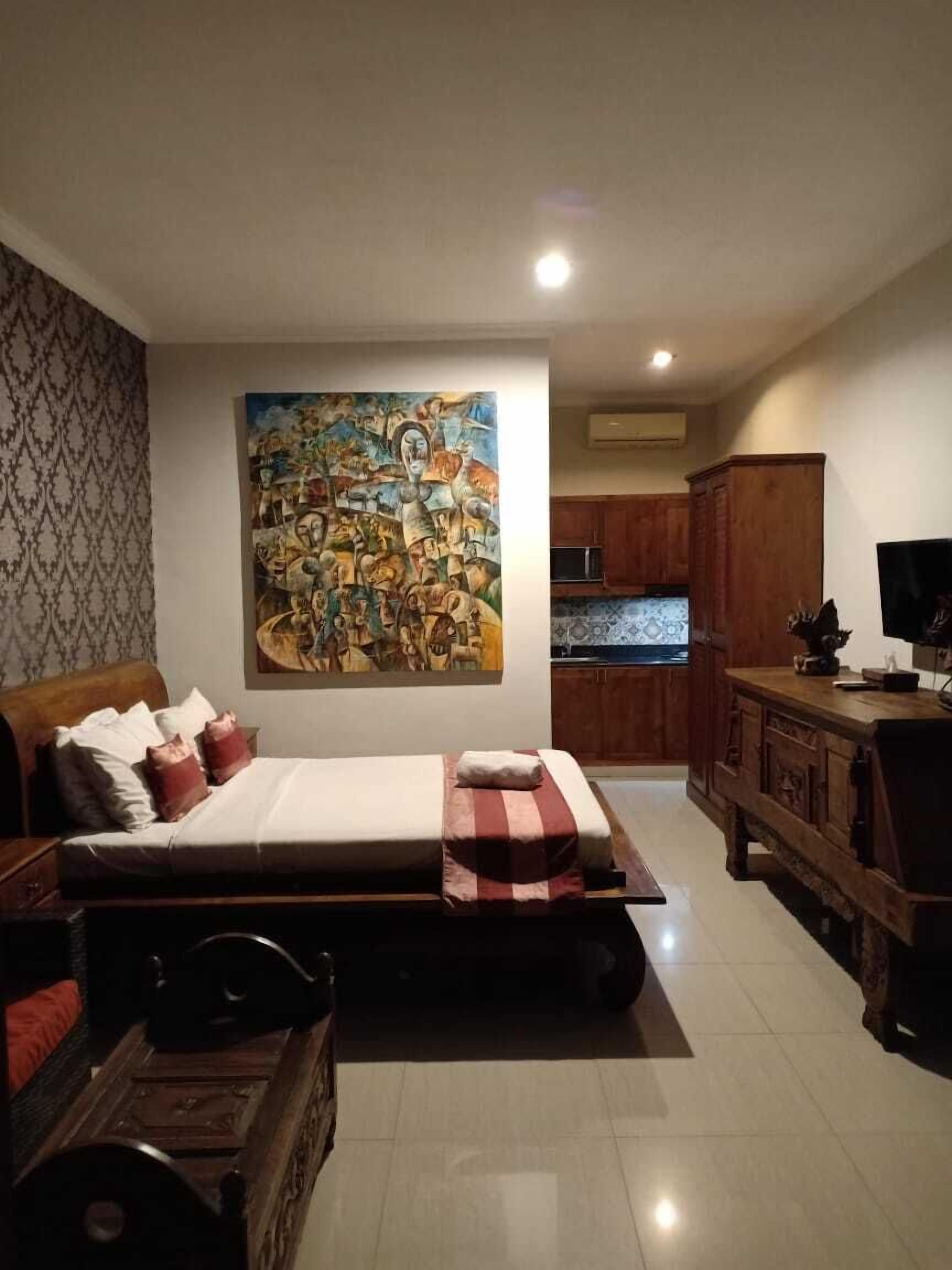 Een slaapkamer met een groot bed, een houten dressoir, een televisie en een keuken in de achtergrond.