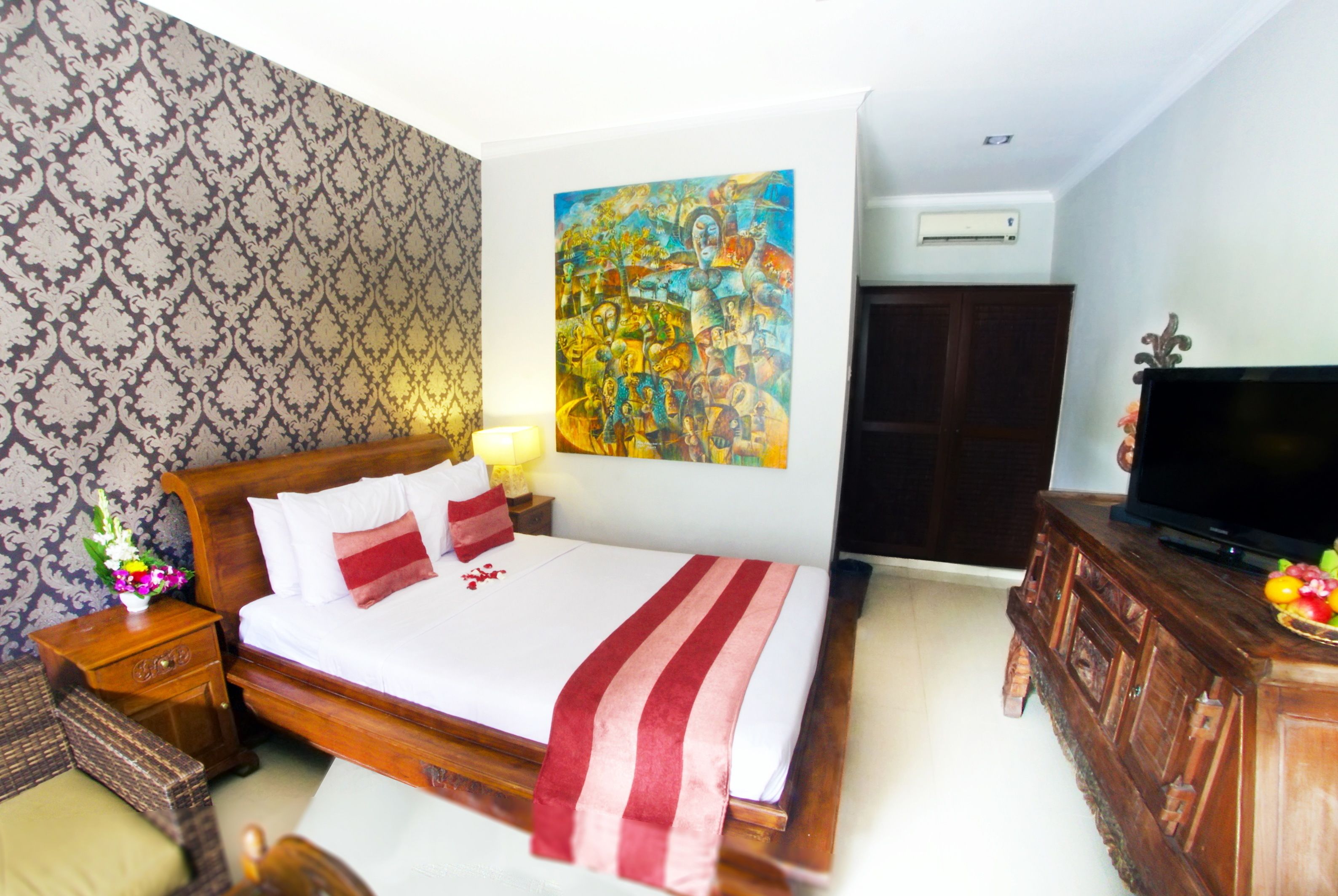 A hotel room with a bed, a nightstand with a lamp, a painting on the wall, a television on a wooden cabinet, and a patterned wallpaper.