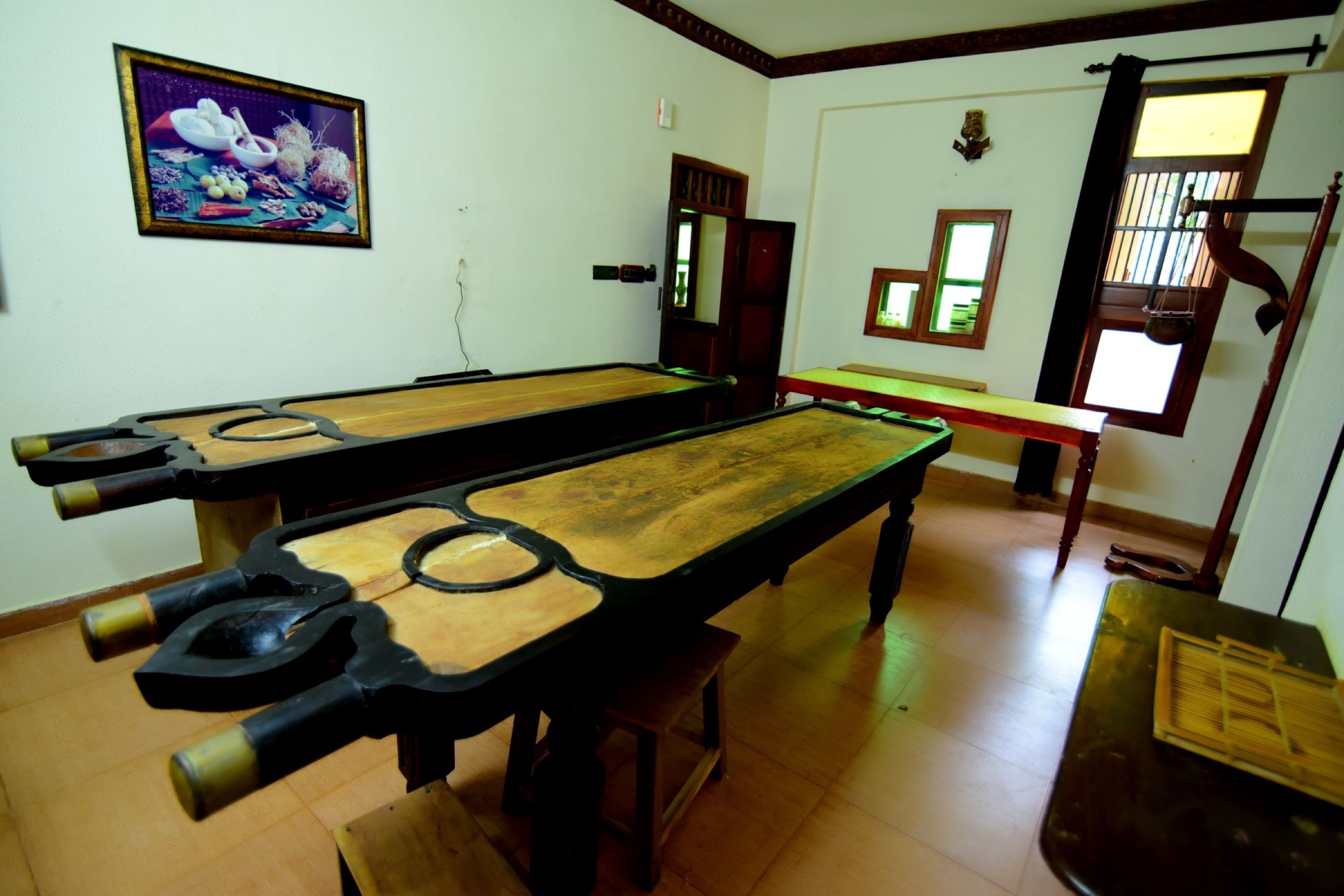 A billiards room with two long tables, a wooden floor, and a framed picture on the wall.