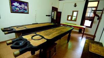 A billiards room with two long tables, a wooden floor, and a framed picture on the wall.
