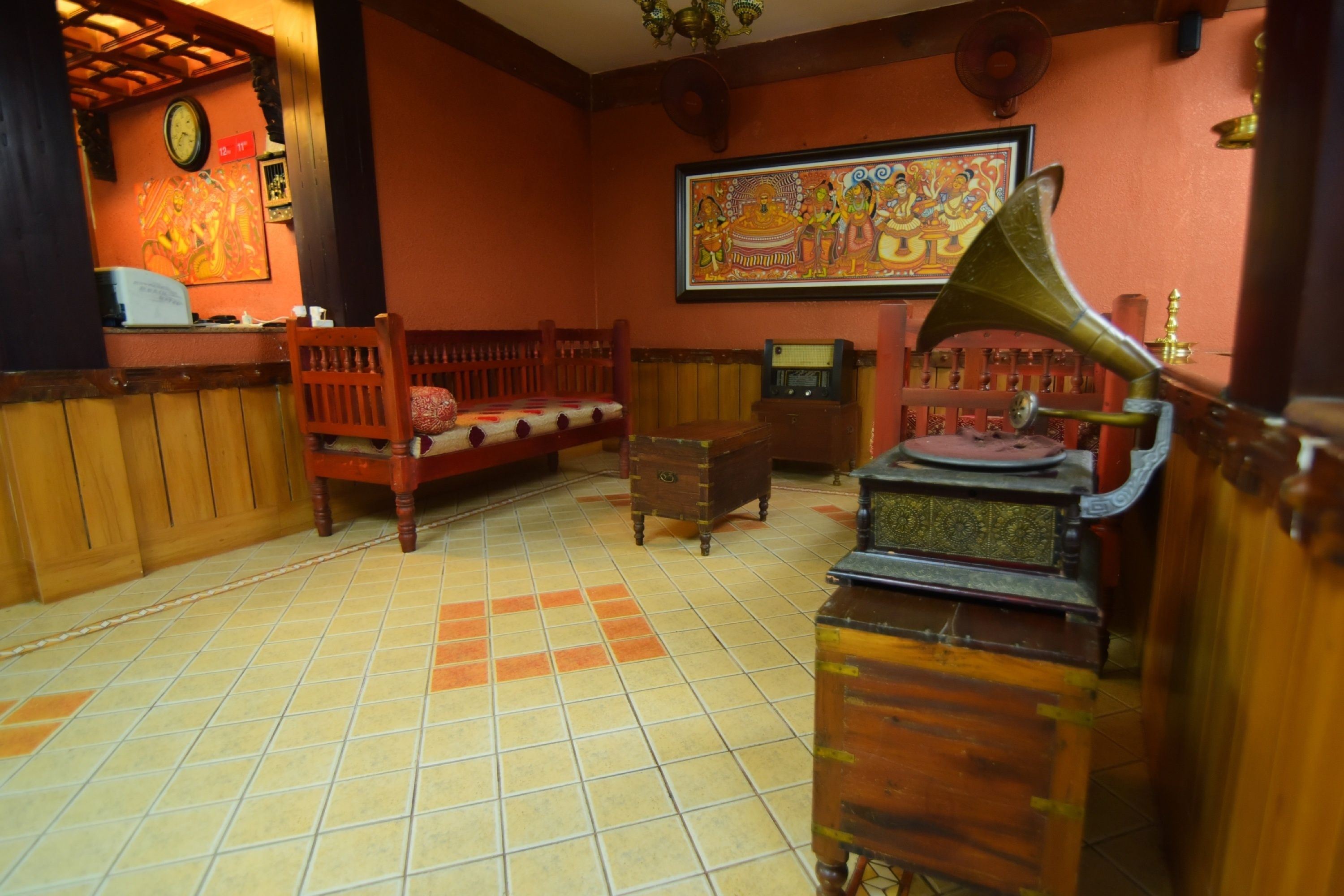 A room with a wooden bed, a small table with a radio, a clock on the wall, and a framed painting.
