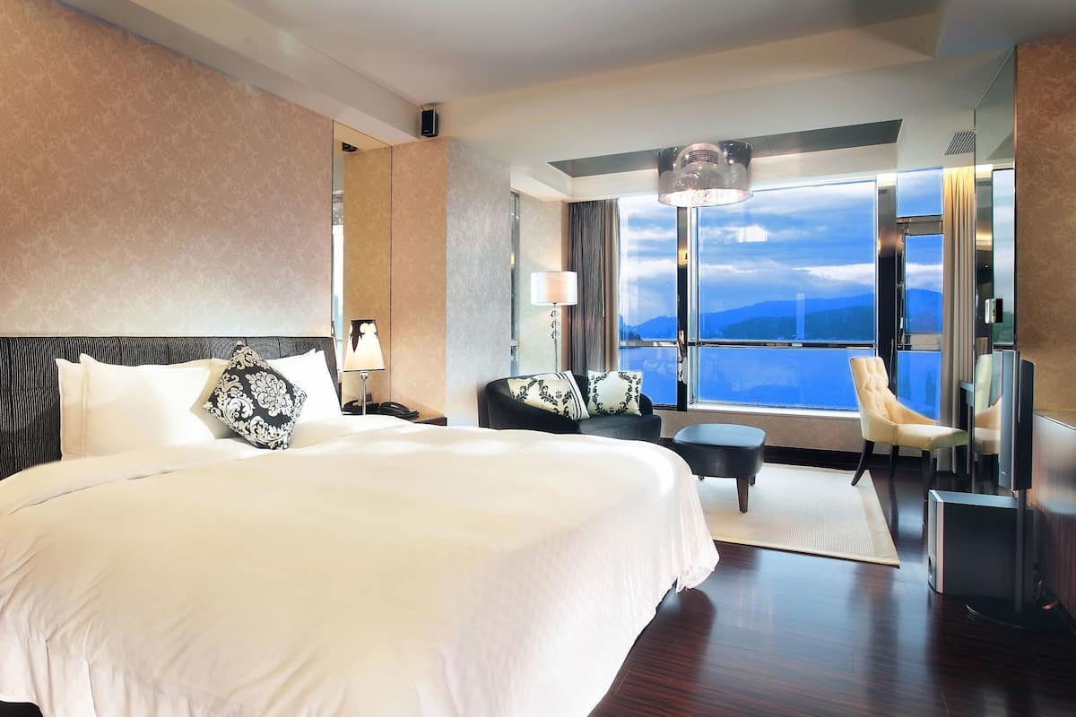 A hotel room with a large bed, a desk, a chair, and a view of the mountains.