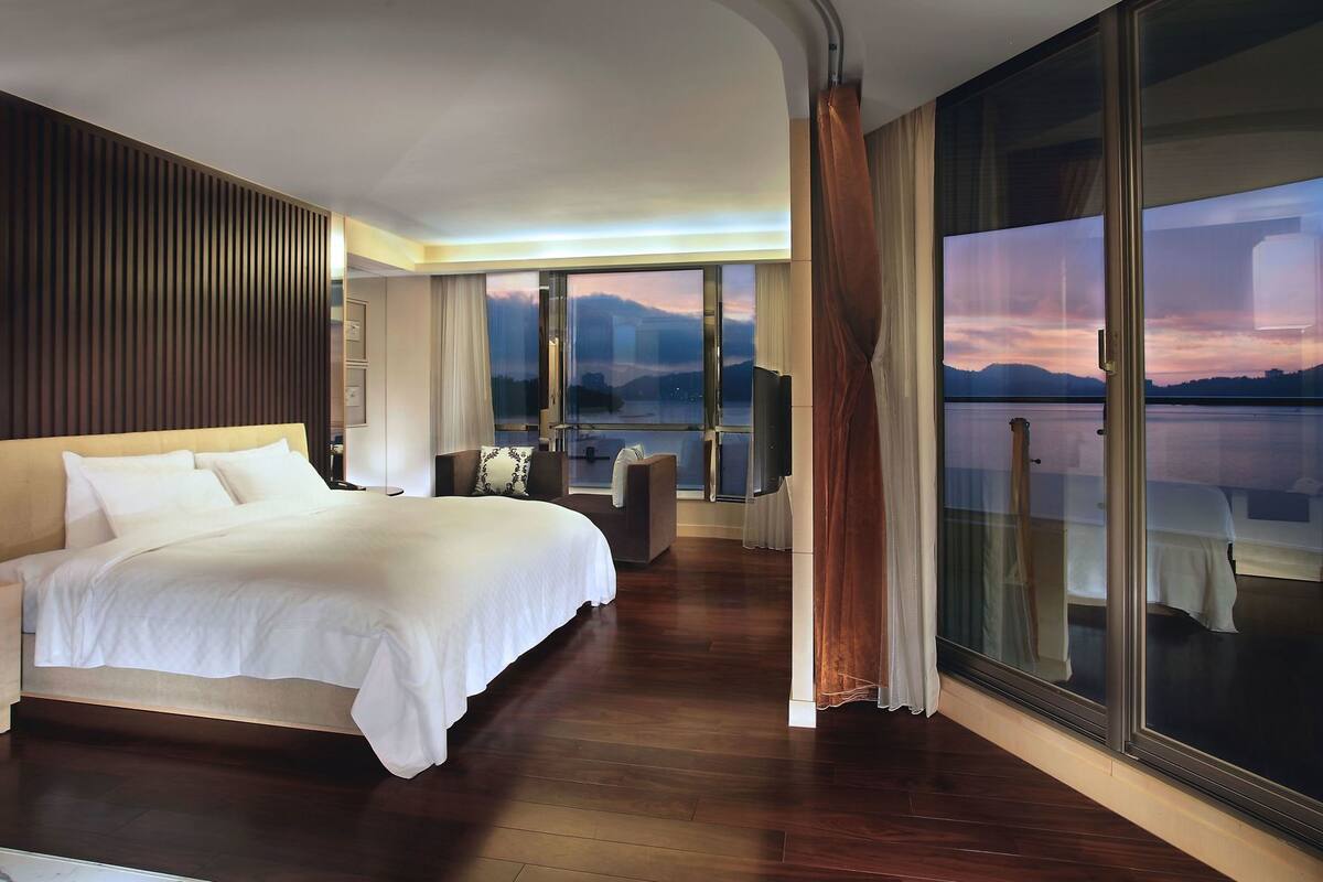 A hotel room with a large bed, a seating area, and a view of a body of water.