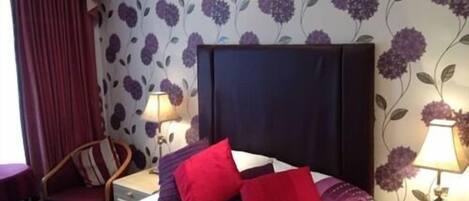 A hotel room with a large bed, two bedside tables, a chair, and floral wallpaper.