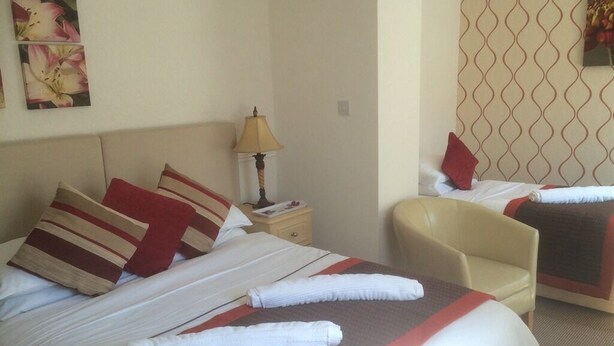 A hotel room with a large bed, a smaller bed, a chair, a nightstand with a lamp, and a wall with a patterned wallpaper. - Pelham Lodge (Blackpool)