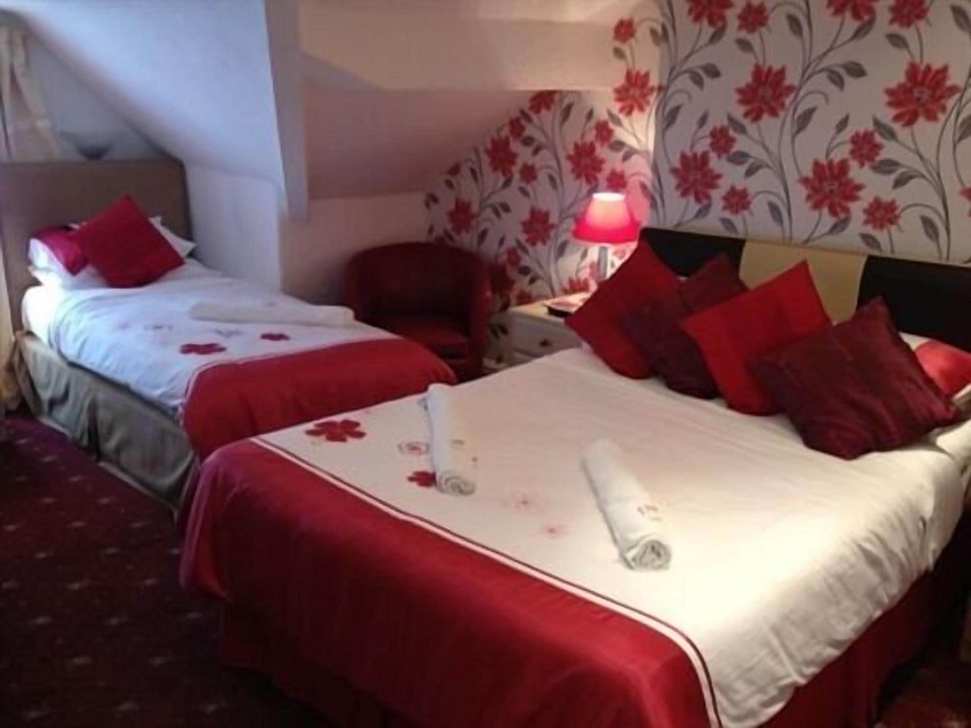 A hotel room with two beds, red bedding, a floral wallpaper, and a red lamp on the nightstand.
