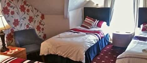 A hotel room with two beds, a chair, a nightstand, and a window with curtains.