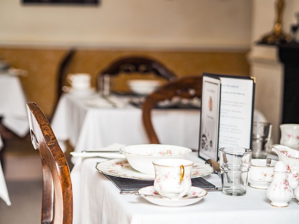 A dining table set with white plates, a floral cup, and a menu stand.